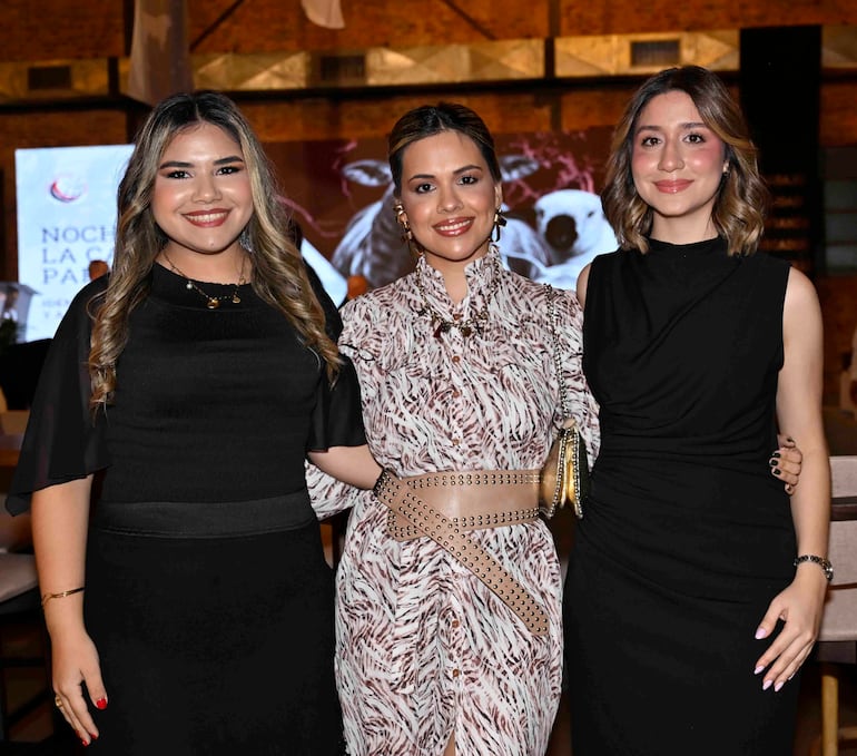 Tres mujeres sonríen a la cámara, vestidas de negro y con estampados, en un ambiente elegante.