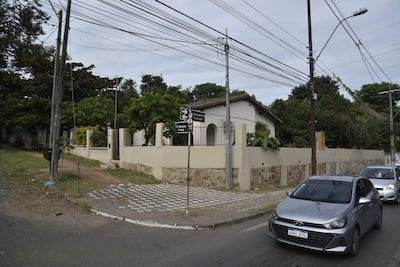 Vista de una calle con pavimento en forma de ajedrez, árboles y una casa blanca, en un día nublado.