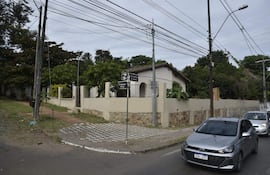 Vista de una calle con pavimento en forma de ajedrez, árboles y una casa blanca, en un día nublado.