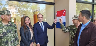 Cinco personas en evento inaugural con bandera paraguaya: generales en uniforme y una mujer sonriente en chaqueta negra.