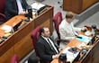 Gustavo Leite en traje negro, Santiago Amarilla Ríos con saco claro sosteniendo un recipiente, Susy Delgado concentrada en su móvil en un recinto legislativo.