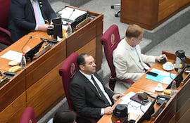 Gustavo Leite en traje negro, Santiago Amarilla Ríos con saco claro sosteniendo un recipiente, Susy Delgado concentrada en su móvil en un recinto legislativo.