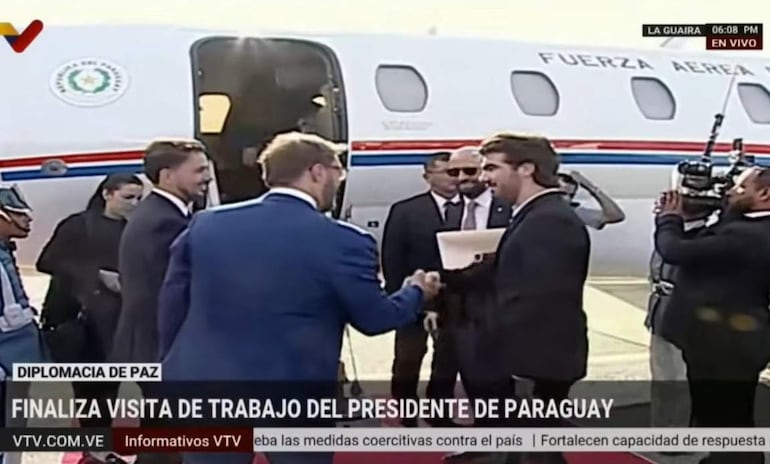 Lautaro Cuevas estrecha la mano de Félix Plasencia, ambos vestidos formalmente, junto a un avión de la Fuerza Aérea Paraguaya.
