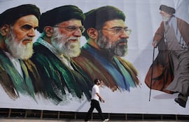 Un hombre pasa frente a una valla en la que aparecen los retratos del nuevo líder supremo de Irán, el ayatolá Mojtaba Jamenei, el difunto líder supremo, el ayatolá Ali Jamenei, y el difunto líder supremo, el ayatolá Ruhollah Jomeini, en Srinagar (India).