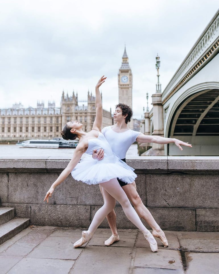 Bailarina en tutú blanco y bailarín en camiseta blanca, ejecutando una elegante pose de ballet junto al río en Londres.