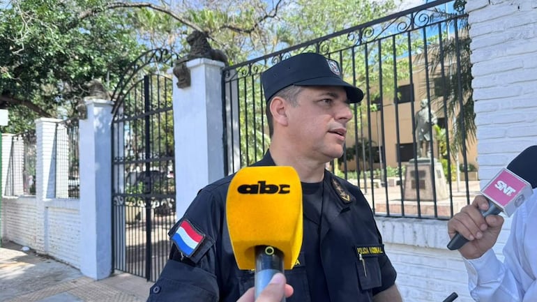 Policía con uniforme y sombrero habla serio, mientras un micrófono amarillo capta la entrevista y otra persona toma notas.