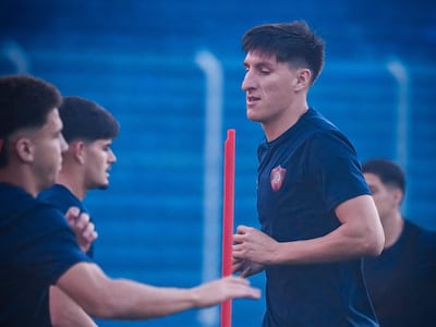 Cuatro futbolistas en camisetas oscuras entrenan en un campo, uno charla mientras otro realiza un ejercicio.