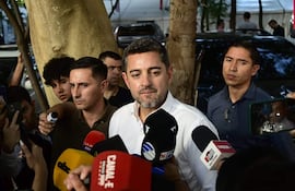 Pedro Alliana con camisa blanca y barba, rodeado de tres hombres, en una conversación con periodistas en un entorno urbano.