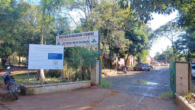 Entrada de la Escuela Básica N° 2647 con carteles del Ministerio de Educación y un camino de grava flanqueado por vegetación.