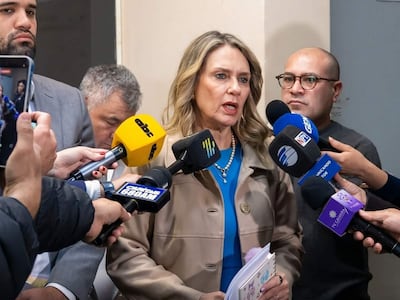 Rocío Vallejo con chaqueta clara y collar, rodeada de periodistas. Hombre con cámara a su izquierda y otro con micrófono a su derecha.