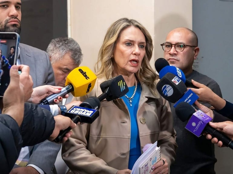 Rocío Vallejo con chaqueta clara y collar, rodeada de periodistas. Hombre con cámara a su izquierda y otro con micrófono a su derecha.
