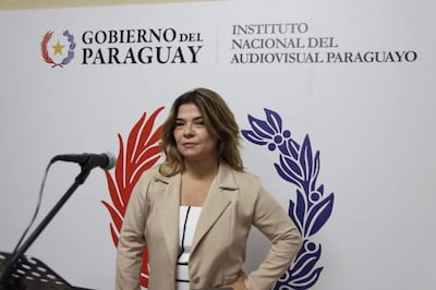 Natalia Fuster Cascio con chaqueta beige y blusa blanca, de pie frente a un fondo institucional del Gobierno del Paraguay.