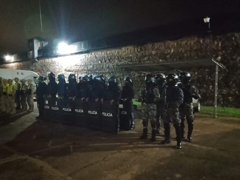 Grupo de oficiales de policía en uniforme táctico, resguardando un procedimiento de traslado de mujeres privadas de su libertad.