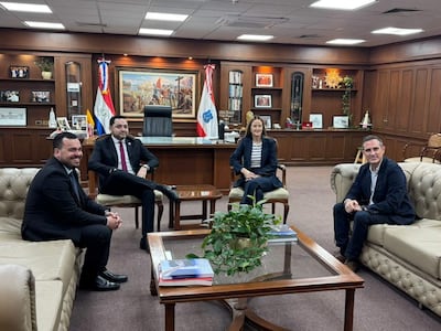 Soledad Núñez con blusa de rayas y pantalones oscuros, Luis Bello en traje negro, en una oficina conversando con sonrisas.