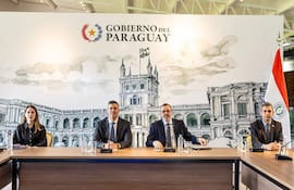 Santiago Peña con traje oscuro, Juan José Galeano vestido de blanco, en reunión formal rodeados de ilustraciones del Palacio de López.