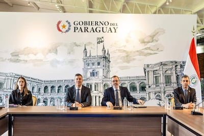 Santiago Peña con traje oscuro, Juan José Galeano vestido de blanco, en reunión formal rodeados de ilustraciones del Palacio de López.