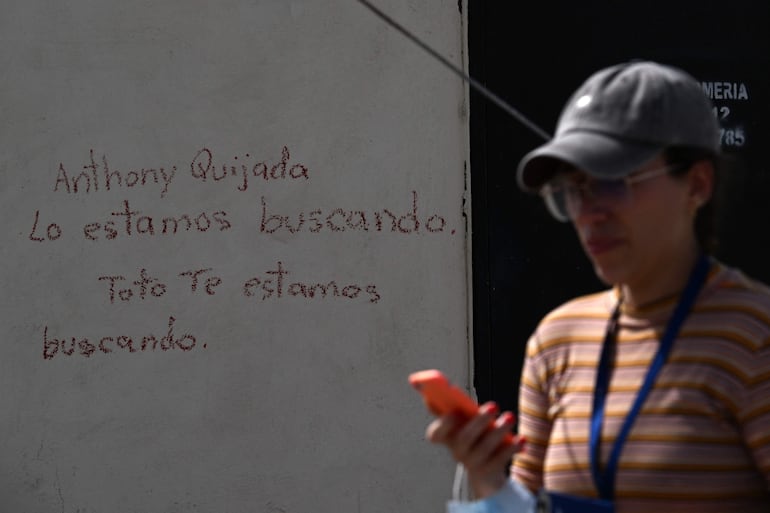 Una persona mira un teléfono móvil junto a una pared con mensajes escritos a mano sobre personas desaparecidas tras los terremotos en Caraballeda, estado La Guaira, Venezuela.