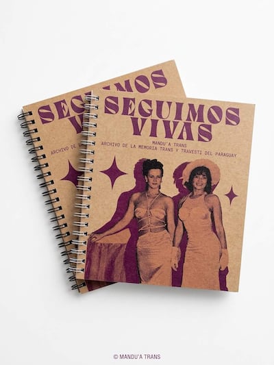 Cuadernos encuadernados con espiral, fondo marrón y texto morado que dice 'Seguimos Vivas', exhibidos sin personas visibles.