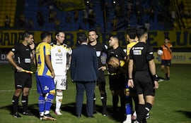El árbitro del partido que no se puso en marcha, Derlis Benítez en conversación con sus colaboradores y los futbolistas de ambos elencos, Fernando Benítez y Fernando Fernández, tras el bochornoso suceso en Capiatá.