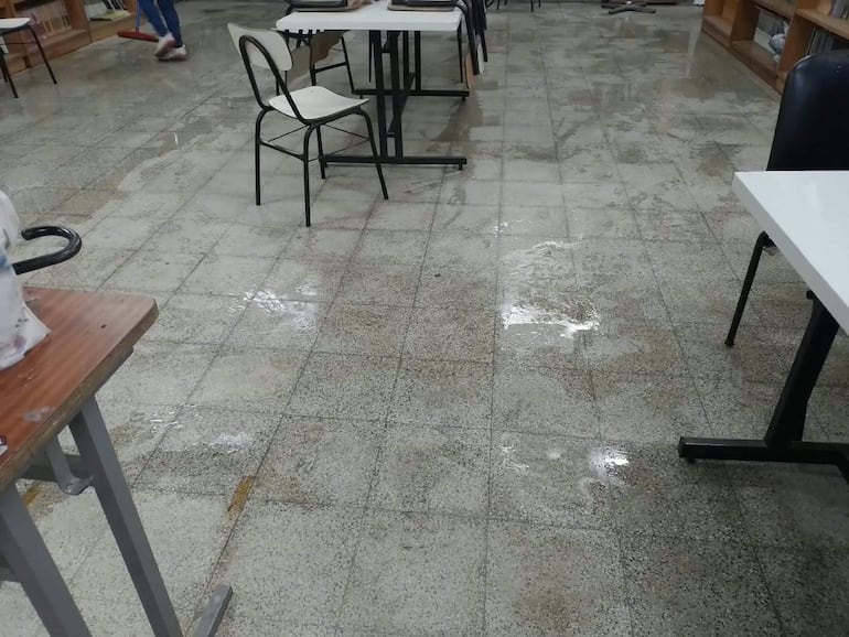 Persona barriendo piso mojado en aula desordenada del Colegio Nuestra Señora de la Asunción tras temporal.