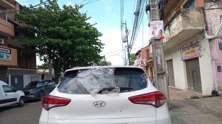 Vehículo Hyundai blanco con ventanilla trasera cubierta por plástico, en un entorno urbano con edificios y vegetación.