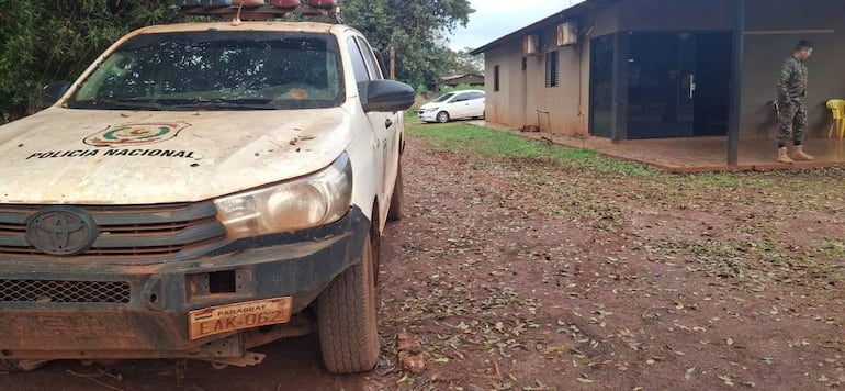 Hombre vestido con uniforme militar espera junto a un vehículo de la Policía Nacional paraguaya en un entorno rural.