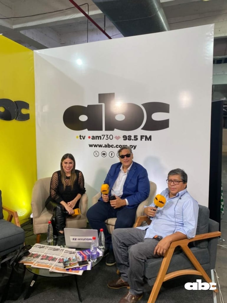 Letizia Medina con blusa negra y micrófono, Diego Marini en traje azul y gafas, y Víctor Ríos en camisa clara, en set de televisión colorido.