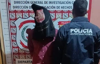 Hombre encapuchado entre policías en sede de investigación, uno lleva chaqueta marcada con 'POLICÍA INVESTIGACIONES'.