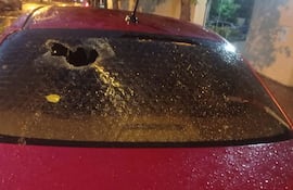 Coche rojo con luneta trasera rota y restos de agua en ambiente húmedo tras granizo.