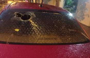 Coche rojo con luneta trasera rota y restos de agua en ambiente húmedo tras granizo.