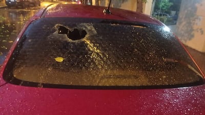 Coche rojo con luneta trasera rota y restos de agua en ambiente húmedo tras granizo.