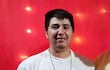 Aldo Alexis Duarte sonriente, en camiseta blanca con el texto 'Keep it Real', fondo rojo decorado con luces.