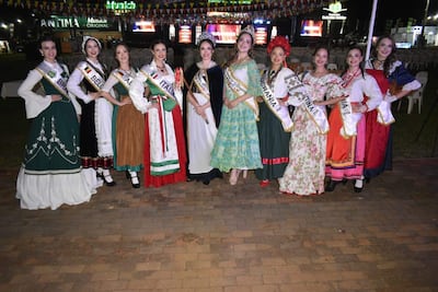Ocho mujeres sonrientes con trajes de Brasil, Bélgica, Italia, Ucrania, y Argentina en un evento iluminado por luces artificiales.
