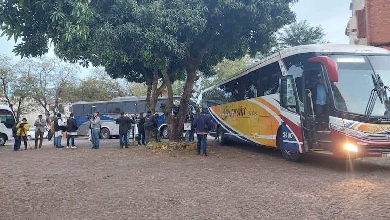 Grupo de médicos reunido en un patio, dos autobuses al fondo, mientras algunos registran en dispositivos móviles.