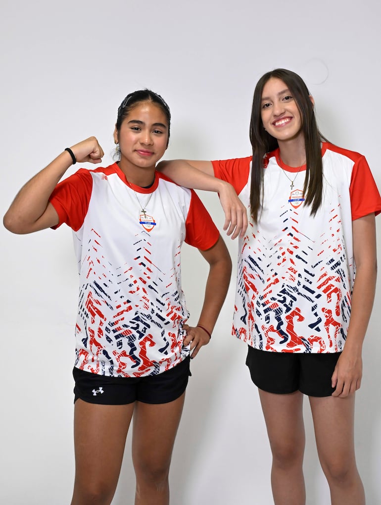Sofía Martínez con camiseta roja flexionando el brazo y Estefaía Gómez sonriendo, ambas vestidas con colores de un equipo en ambiente interior.