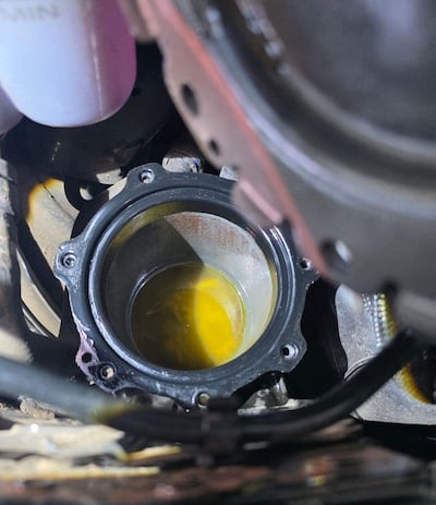 Vista del interior de un motor en taller mecánico con receptáculo de líquido amarillo, posiblemente aceite, y componentes metálicos.