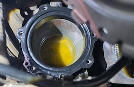 Vista del interior de un motor en taller mecánico con receptáculo de líquido amarillo, posiblemente aceite, y componentes metálicos.