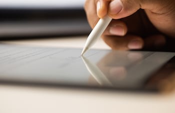 Primer plano de la mano de un empresario firmando electrónicamente un contrato en una tableta con un lápiz óptico.