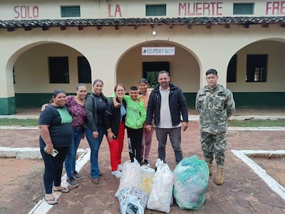 Siete personas frente a un edificio, entre ellas un niño y dos mujeres sonriendo, con bolsas de donaciones en el suelo.