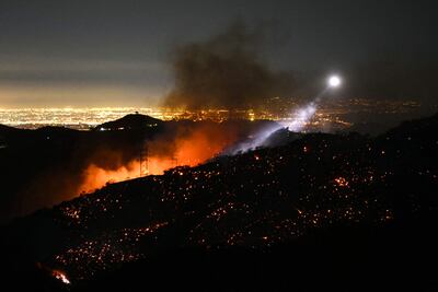 La luz de un helicóptero de extinción de incendios ilumina una ladera humeante mientras el incendio de Palisades crece cerca del vecindario de Mandeville Canyon y Encino, California.