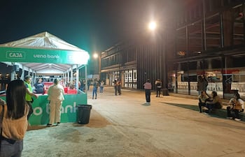 Grupo de personas bajo carpa de ueno bank, conversando en evento nocturno, con luces artificiales y ambiente festivo.