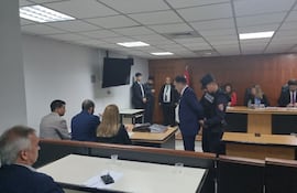 El senador Edgardo Kueider ingresó a la sala de juicios con esposas y las manos atrás. Justamente un policía le quita las esposas antes de iniciar el debate. La otra acusada, Iara Guinse ya está sentada.