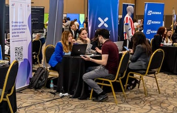 Mujer de chaqueta azul y hombre de camiseta burdeos conversan en feria de empleo, rodeados de banners de Manpower y Kemsa.
