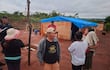 Tres hombres, dos en uniforme policial, y tres mujeres, una con un niño, en un entorno rural marcado por tierra roja y vegetación escasa.