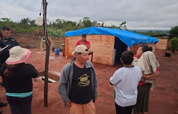 Tres hombres, dos en uniforme policial, y tres mujeres, una con un niño, en un entorno rural marcado por tierra roja y vegetación escasa.