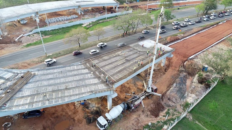 Diez trabajadores manipulan varillas de acero en el montaje de un viaducto en construcción, con maquinaria y materiales visibles alrededor.