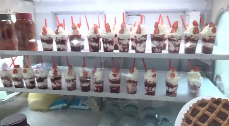 Vasos de helado y crema decorados con cerezas, dispuestos en estantería de feria de postres.
