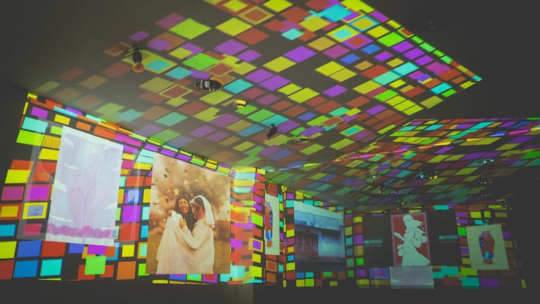 Ambiente interior vibrante con proyecciones de arte gráfico en grandes paneles y colores geométricos.