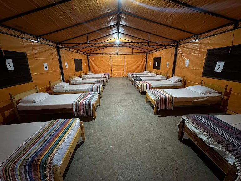 Interior de albergue con diez camas individuales y colchas multicolores en un ambiente organizado y sin personas.