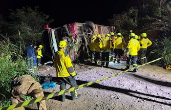 Rescatistas en uniformes amarillos rodean un camión volcado en la maleza, organizándose para ayudar en la escena del accidente.